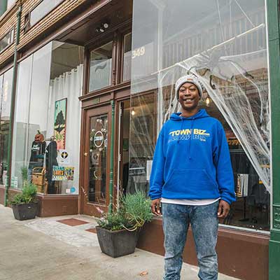 A woman wearing a blue Town Biz sweatshirt stands outside the store in Oakland, California