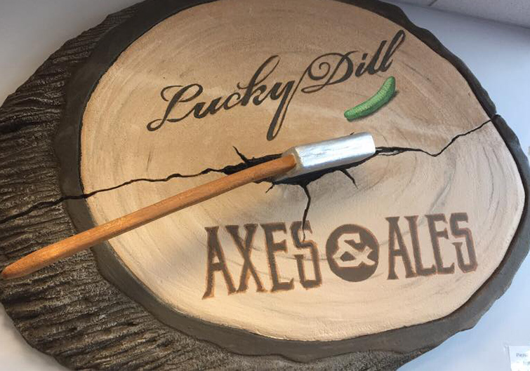 A sign designed to look like a split trunk with an axe sticking out labeled “Lucky Dill Axe and Ales”