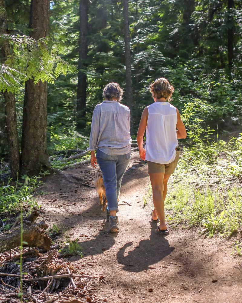 two women walk a dog on a forested trail