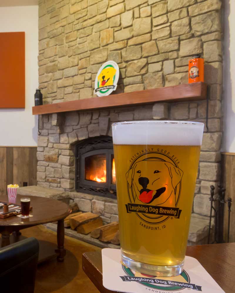 a glass of craft beer sits on a table with a fireplace in the background