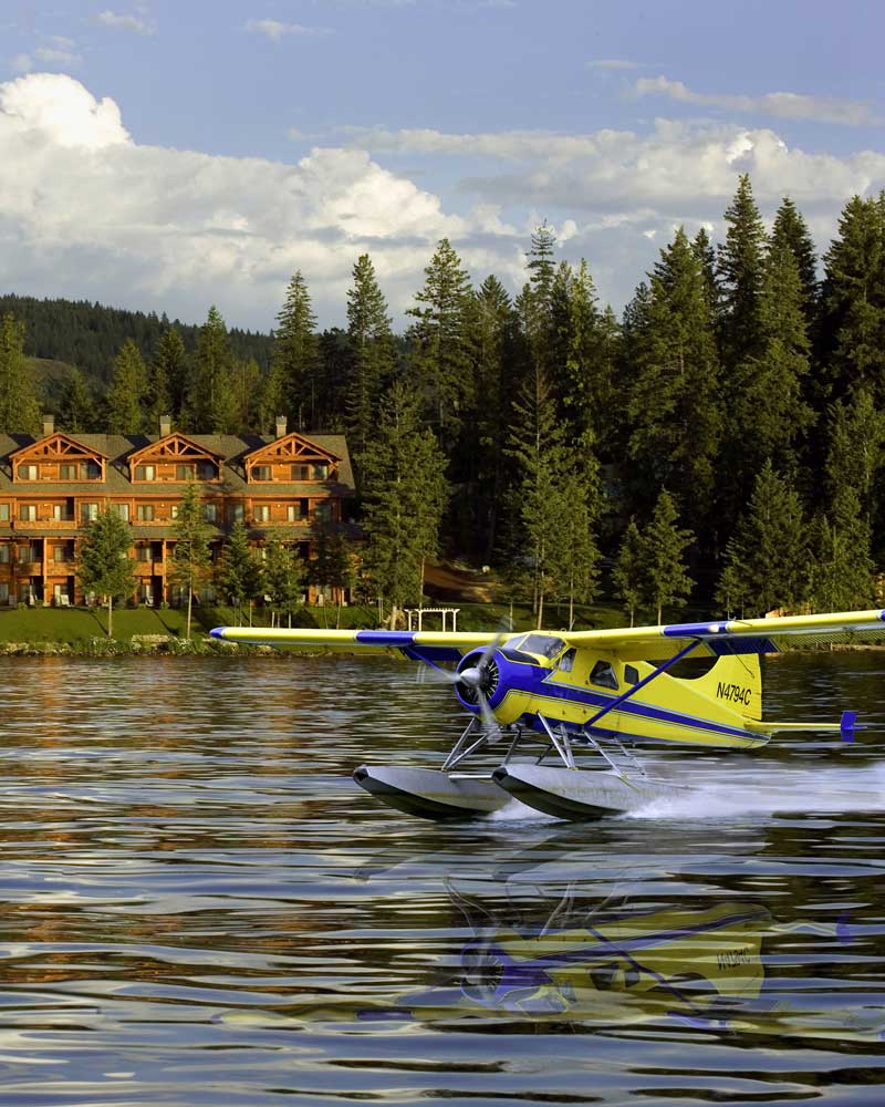 a sea plane lands on a lake with a lodge-style resort in the background