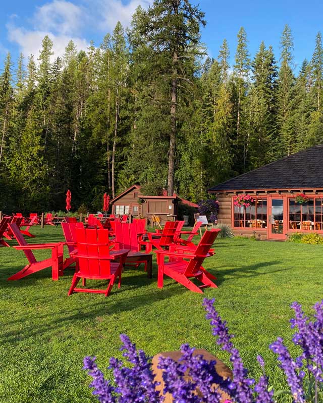  red chairs sit on a lawn along the shores of a lake
			