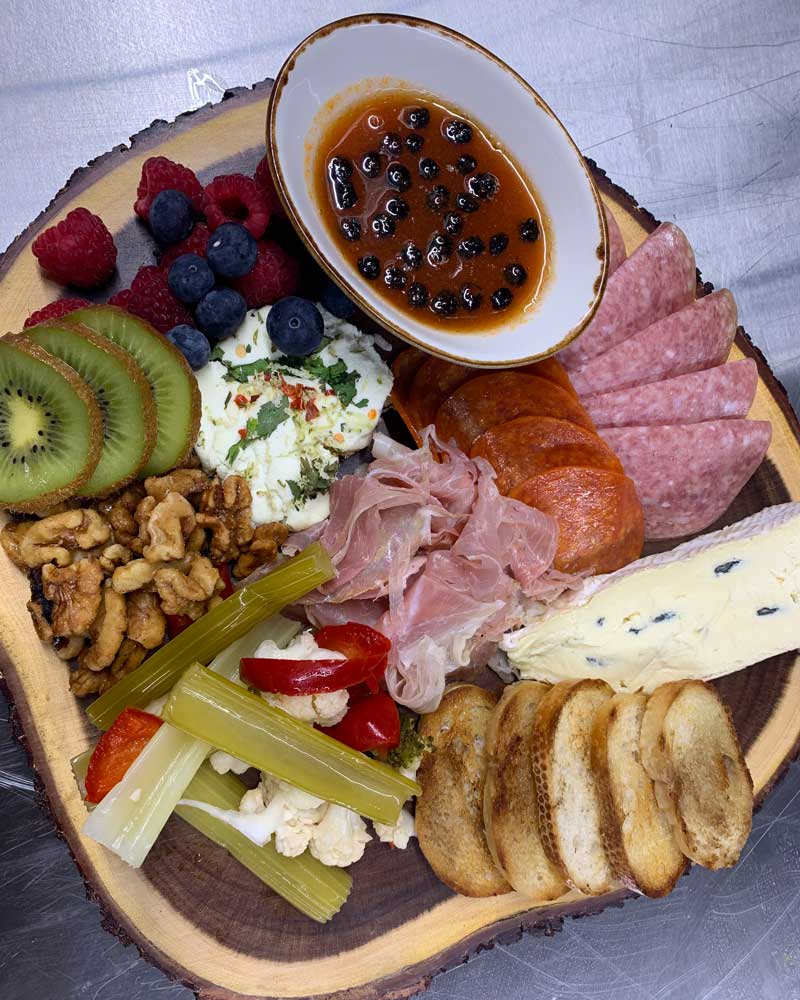 : a rustic plate topped with fruits, cheeses, meats and jams. 
				
