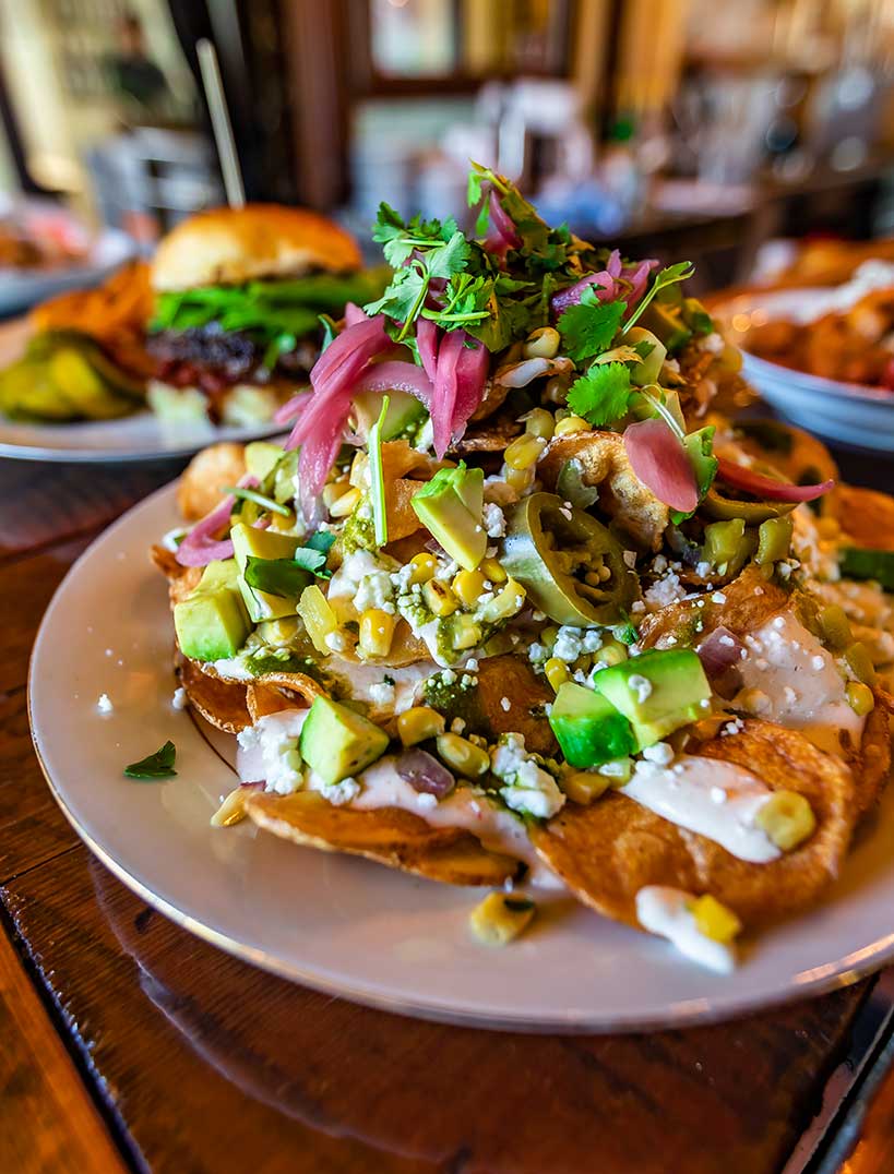a pile of nachos dressed in avocados, jalapenos, pickled onions and corn