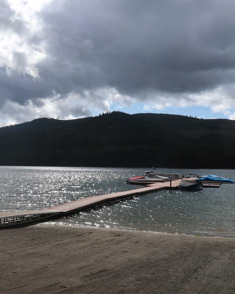a dock stretched over a lake with boats around it 
			