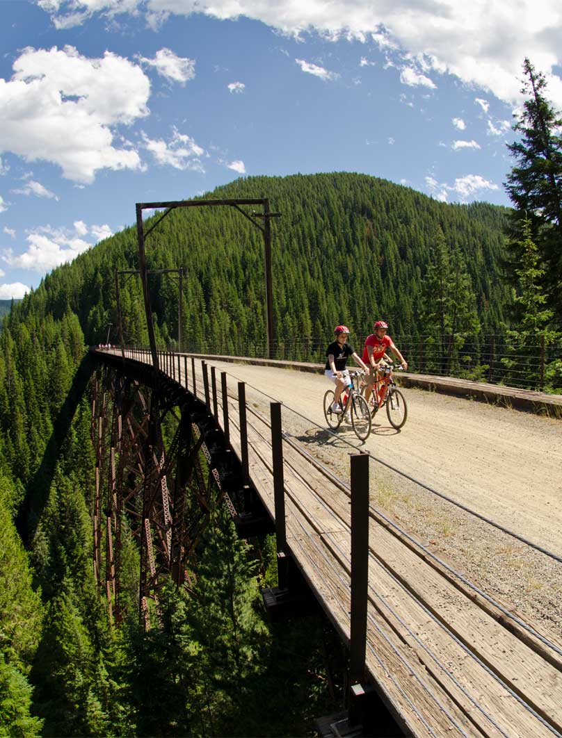 a man and woman ride bikes on a converted railroad line trestle bridge 
				