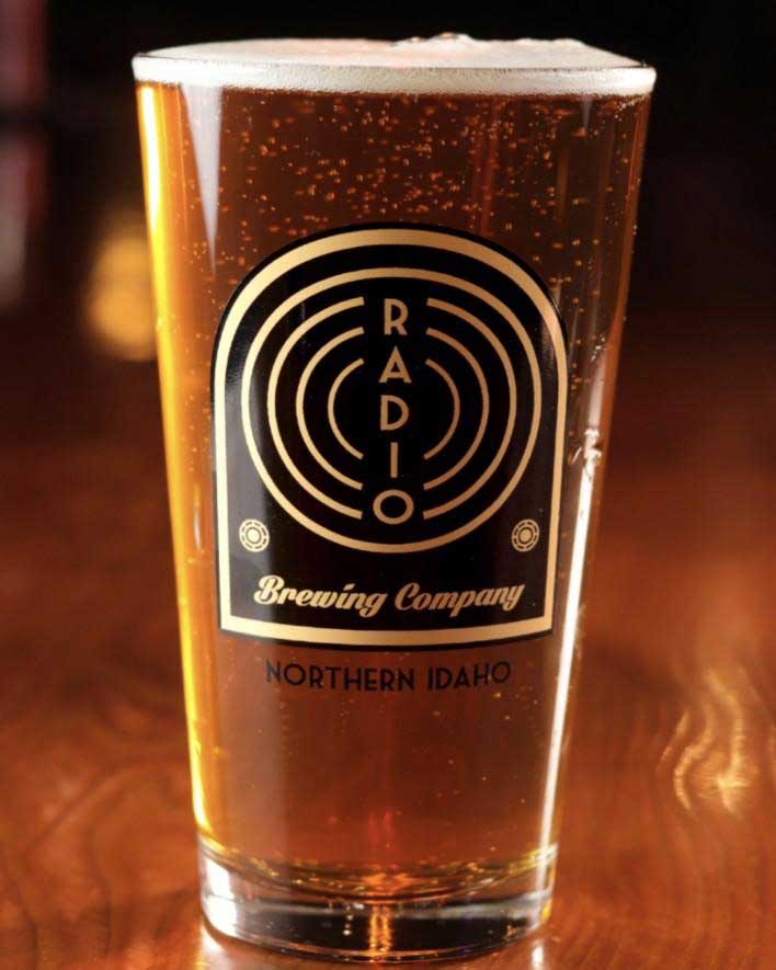 a pint of beer with an old fashioned radio mic logo on the glass