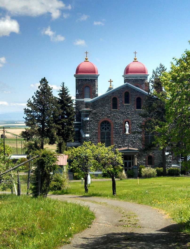 a monastery at the end of dirt road, surrounded by grass and trees 